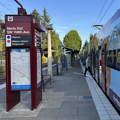"The Merlo Road transit center with wayfinding sign and a person getting on the MAX.""
